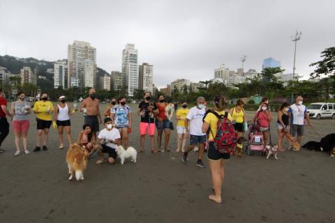 tutores de cães, com alguns animais posam em conjunto para foto na faixa de areia. #paratodosverem
