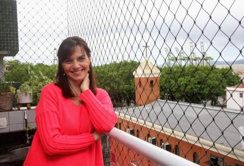 a jornalista Camilla Costa, na varanda de casa, com a torre da igreja ao fundo. #paratodosverem
