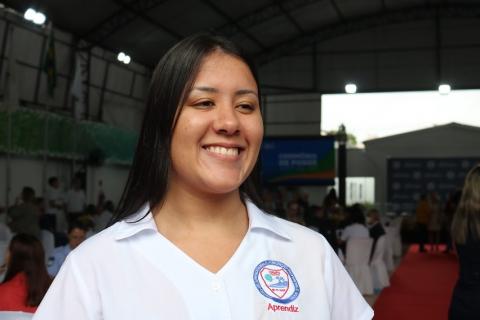 maria Júlia, com a camisa do camps, está sorrindo. Ao fundo, movimentação de pessoas. #paratodosverem