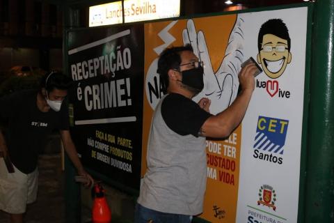 Homem prende cartaz no ponto de ônibus #paratodosverem