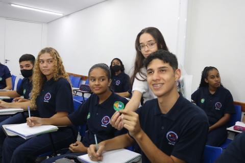 aprendizes estão sentados. Um deles exibe um sele de propaganda de campanha. #paratodosverem