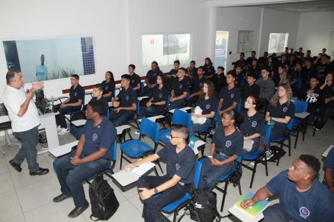 jovens estão sentados, de frente para a foto, assistindo a palestra. Homem fala a todos. #paratodosverem