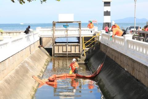 Barreira e homens trabalhando dentro do canal junto à orla. Comporta está fechada. #paratodosverem