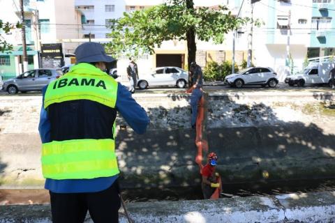 Fiscal do ibama, com colete de identificação está de costas para a foto. Ao fundo, homens instalam barreira na parte interna do canal. #paratodosverem