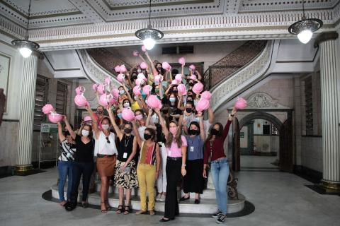 Mulheres exibem capacetes rosa no saguão do paço municipal. #pratodosverem