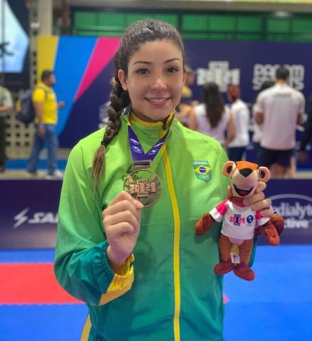 atleta segura medalha e mascote de pelucia dos jogos #paratodosverem