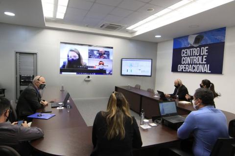 Várias pessoas em uma mesa olhando para um telão. #paratodosverem