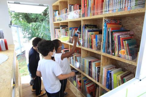 Crianças escolhem livros em estante na carreta. #paratodosverem