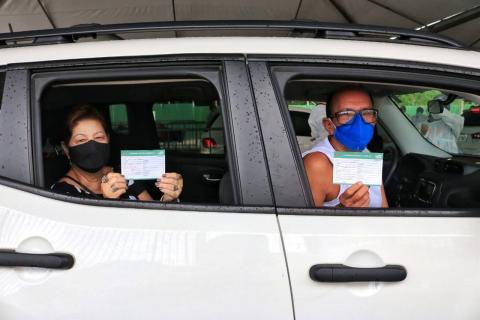 casal exibe comprovante de vacina dentro de carro. A mulher está no banco de trás e o homem, no da frente. #paratodosverem