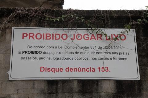 Placa de proibição de jogar lixo afixada em muro. #paratodosverem