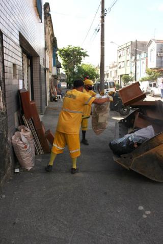 homens uniformizados recolhem caixas e material de madeira encostados em muro. #paratodosverem
