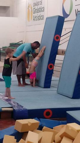 Criança fica de cabeça para baixo sendo orientada por professor na ginástica. #paratodosverem