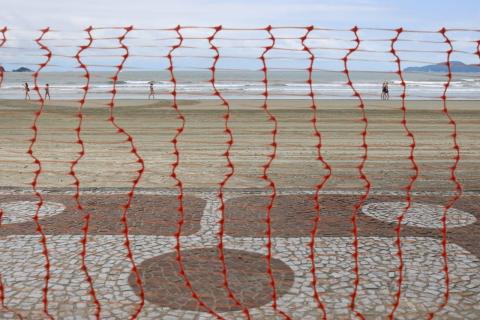 Cerca plástica com a faixa de areia e o mar ao fundo. #Paratodosverem