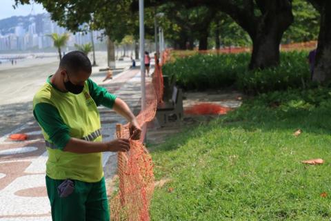 Funcionário instala cerca plástica diante do jardim da orla. #paratodosverem