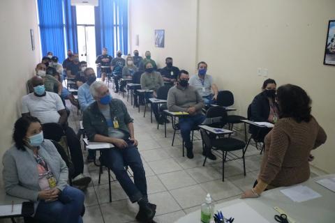 Mulher (de costas) dá palestra para agentes que estão sentados. #paratodosverem