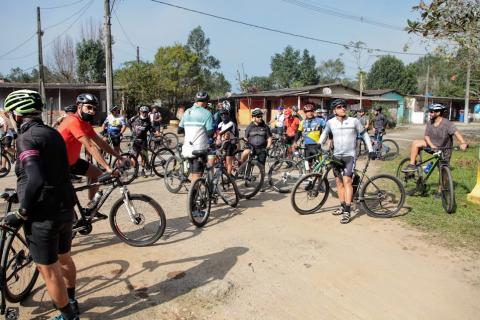 ciclistas chegam ao Vale do Quilombo. Há algumas construção de madeira ao fundo. #paratodosverem