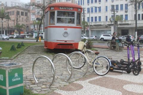 Bicicletário na praça com bonde turístico atrás. #paratodosverem
