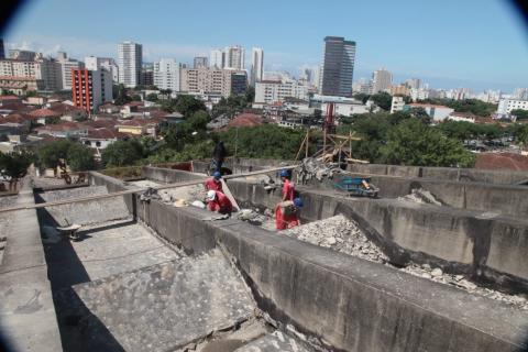 Cobertura em primeiro plano com homens trabalhando ao fundo. #Paratodosverem