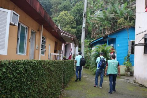 agentes de zoonoses caminham  por rua com sobrados dos dois lados. #paratodosverem