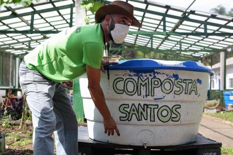 Homem aponta para composteira onde se lê Composta Santos. #Paratodosverem