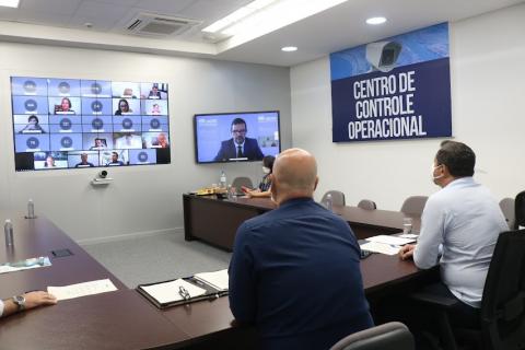 dois homens estão sentados de costas para a foto. Eles olham para telão onde está projeta imagem. #paratodosverem 