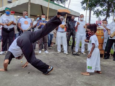 Adulto e criança jogam capoeira em roda montada no evento. #pracegover