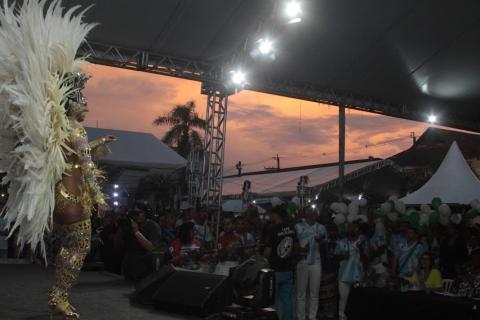 Passista samba no palco com público observando e entardecer ao fundo. #paratodosverem