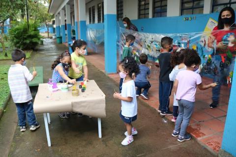 Crianças desenhando em mural no pátio da escola #paratodosverem