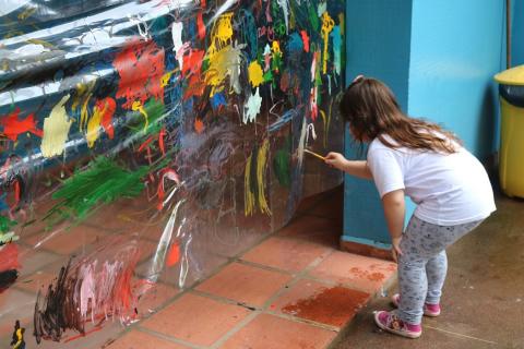 Criança pinta mural de plástico que está todo colorido #paratodosverem