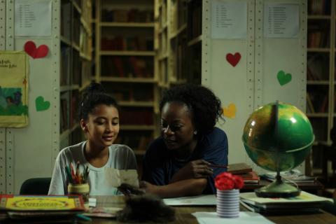 menina está estudando com a mãe na mesa de uma sala. #paratodosverem