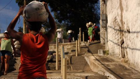 Os carregadores do monte. Homens estão subindo o Monte Serrat com sacos na cabeça. #paratodosverem