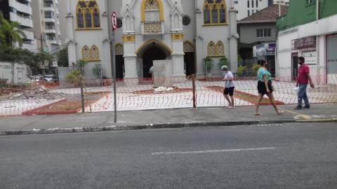 Praça em obras cercada por rede e igreja ao fundo #paratodosverem