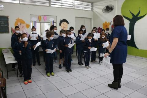 crianças se apresentam em coral, sob orientação de professora. #paratodosverem