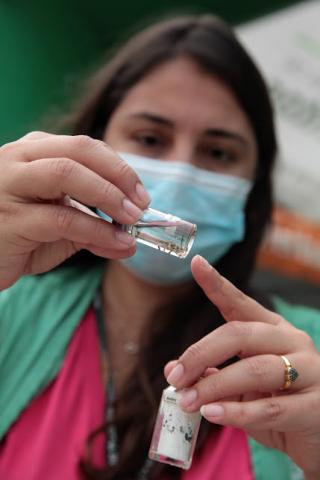 imagem em close de  mulher segurando frascos com larvas de dengue. #paratodosverem