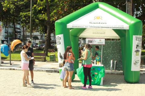 Munícipes recebem orientação de agente em estande educativo. #pratodosverem