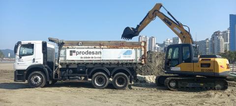 escavadeira remove areia de canal na praia e despeja dentro de caminhão. #paratodosverem