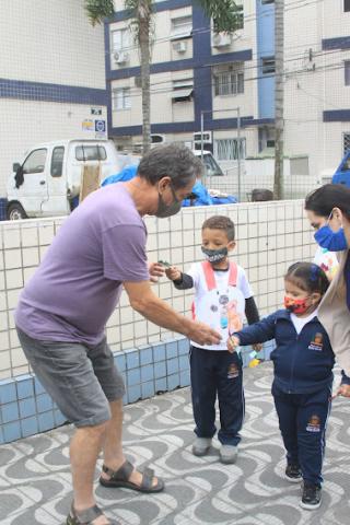 duas crianças entregam flor para homem na calçada. #paratodosverem