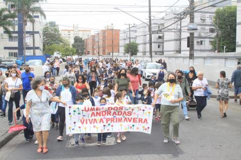 crianças caminham pela pista acompanhadas por adultos e segurando faixa onde se lê UME DOS ANDRADAS VIVA A PRIMAVERA. #paratodosverem