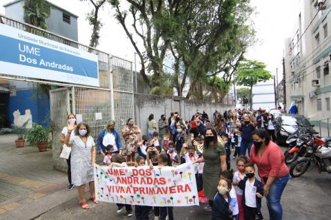 crianças estão na porta da escola segurando faixa. #paratodosverem