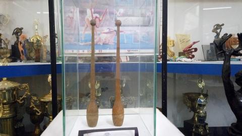 maças de madeira protegidas por redoma de acrílico/vidro. Troféus ao fundo. #paratodosverem
