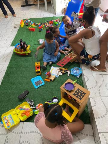 crianças estão sentadas sobre um pequeno tapete se divertindo com brinquedos. #paratodosverem 