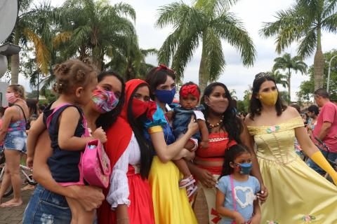 Meninas fantasiadas de princesas posam para fotos com crianças no colo. #paratodosverem