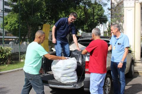 quatro homens estão descarregando caçamba de veículo onde estão pacotes com doações. #paratodosverem
