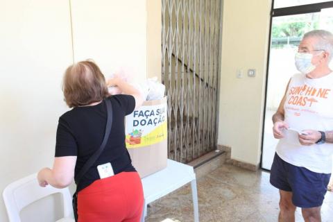 Mulher está de costas para a foto depositando alimentos em caixa de papelão já cheia. #paratodosverem