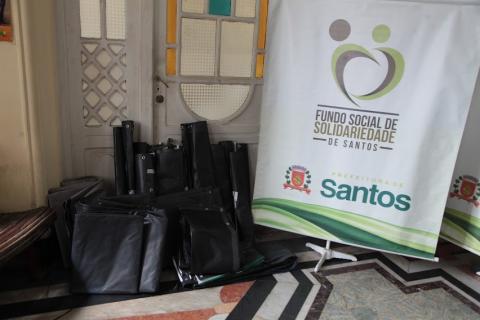 pedaços de lona no chão ao lado do banner do fundo social de solidariedade. #paratodosverem