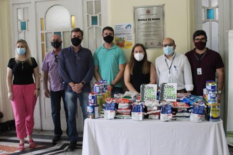 representantes da Gestão e do Fundo Socal posam para foto atrás de mesa com pacotes e latas de leite. #paraotodsverem