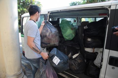 sacos com roupas e alimentos são colocados dentro de uma van por um homem. #paratodosverem