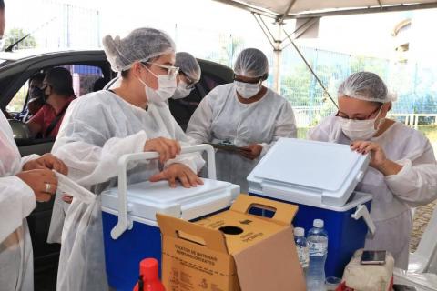 mulheres paramentadas manuseiam caixas térmicas onde ficam as vacinas. #paratodosverem