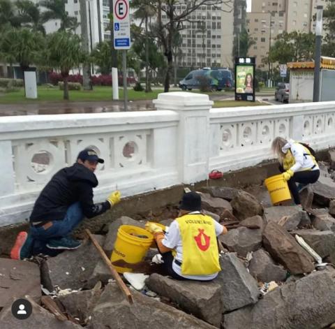 voluntários do grupo ecofaxina entre as rochas da ponta da praia, atrás das muretas, recolhendo resíduos. #paratodosverem 