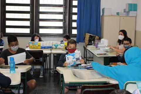 Sala de aula com vários alunos sentados preparando o material #paratodosverem